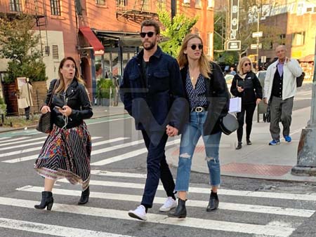 Liam Hemsworth and a mystery girl crossing the streets holding hands.