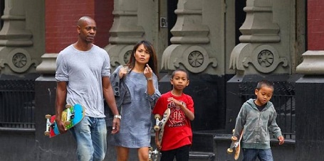 Dave Chappelle carrying a skateboard in his right hand, in blue jeans and grey T-shirt (Far left). Elaine raising her left hand with the index pointed at the camera as she looks shocked or furious at being photographed (second left). Sulayman carrying a skateboard in his right hand as he also has his left hand raised to his neck level in a red T-shirt (second right). Ibrahim looks indifferent to anything as he walks in a patterned hoodie with a skateboard in his right hand (far right).