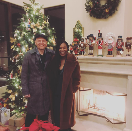 Bill Burr and Nia Renee Hill standing in front of a Christmas tree,