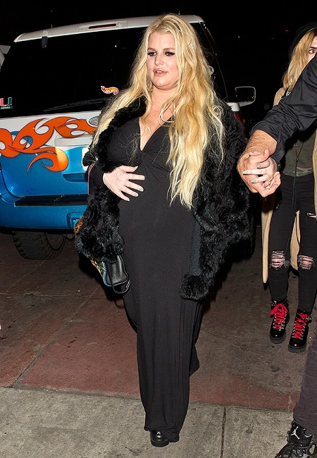 Jessica simpson in a black dress touching her belly during her second pregnancy.