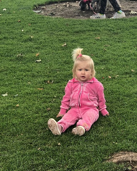 Emeline wearing a pink tracksuit sitting on a green grassfield.