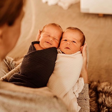 The twin boys in the hands of Bode's mother wrapped in one black and one white towels. The baby in the black towel smiling.