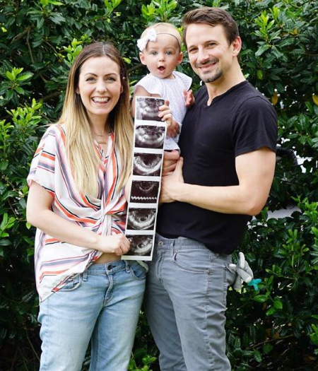 couple and their daughter posing while holding a sonograph. 