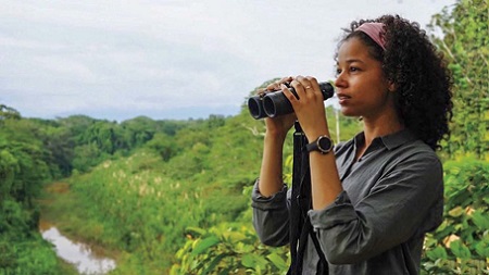 A young Alisha Wainwright holding binoculars just lifted towards her eyes.