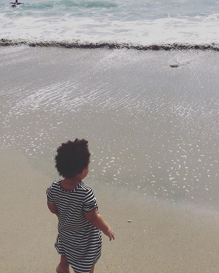 Lola looking at the ocean waves near her on a beach, face not showing.