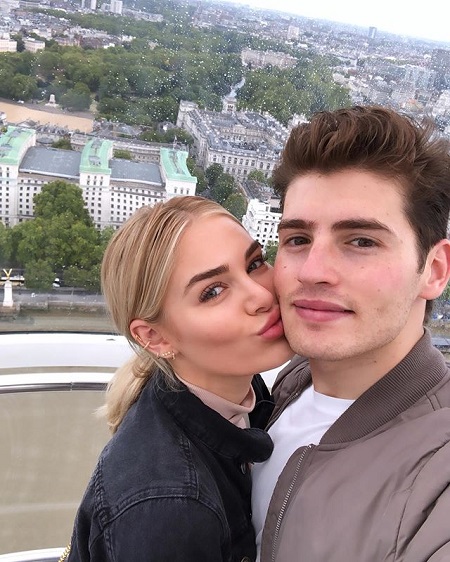 Michelle Randolph kissing Gregg Sulkin on the cheek as he takes the selfie. She too looking at the camera.