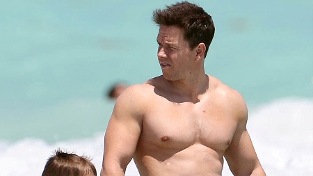 Wahlberg in the beach, shirtless and looking back as he walks with his daughter (not show).