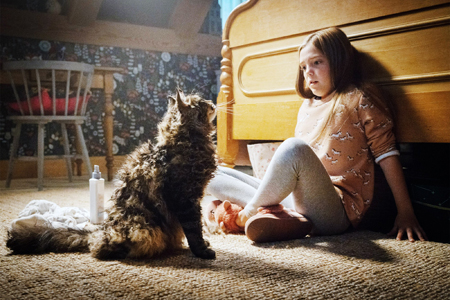 Ellie leans back against the back board of her bed as a cat sits in front of her.