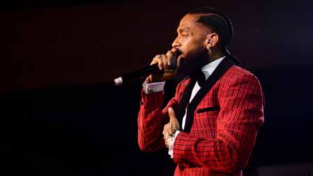 Nipsey Hussle holds a mic to his mouth and other hand to his chest.