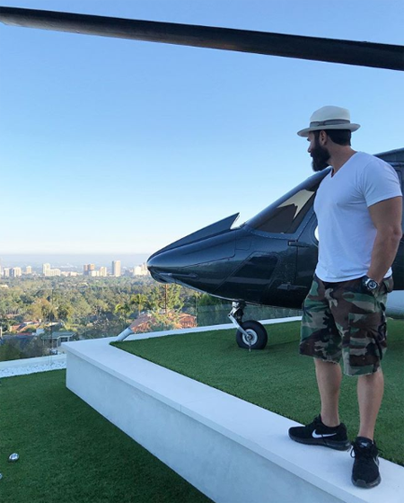 Dan Bilzerian stands beside a helicopter.