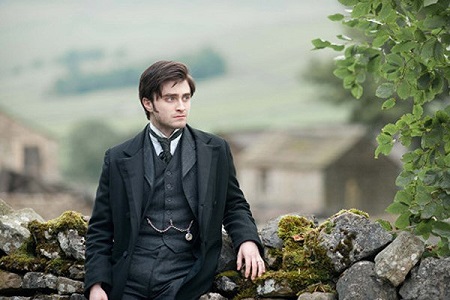 Daniel Radcliffe posing on a stone wall wearing a suit and looking sideways from the camera.