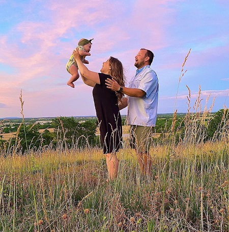 Anna Duggar lifting her daughter in the air as Josh Duggar stands behind her.